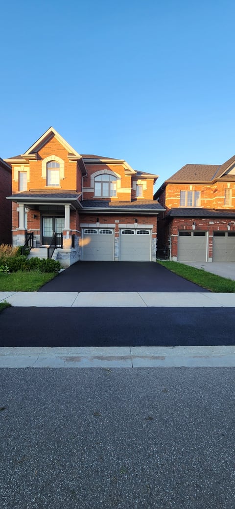 Two-story brick house with orange and red facade, two-car garage, driveway, and clear blue sky in residential neighborhood